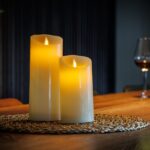 To genopladelige LED-vokslys fra DORSETTO på en flettet dækkeserviet med vin og blødt oplyst baggrund for en hyggelig atmosfære