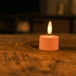 Et sæt med 12 rosa genopladelige fyrfadslys med blød gul LED-flamme og en fjernbetjening står på et træbord. Hvert fyrfadslys kan lyse op til 400 timer og skaber stemningsfuld belysning i hjemmet.
